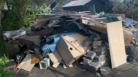 A large pile of timber offcuts, carpet, breeze blocks and old cabinetry stacked by the shed